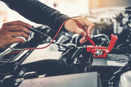 Auto mechanic working on car repair with tools for battery testing